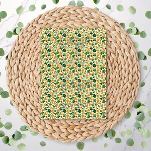 May include: A rectangular item featuring a repeating pattern of green and orange shamrocks on a white backdrop. It's placed on a round, woven, light brown placemat, with scattered green leaves around the edges.