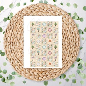 May include: A white card featuring a repeating pattern of palm trees, seashells, and beach-themed illustrations in shades of green, pink, and blue on a beige background. The card is placed on a woven, circular placemat, with scattered green leaves.