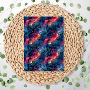 May include: A rectangular fabric with a vibrant, abstract design. The pattern features swirling blues, reds, and golds, resembling a nebula or galaxy. The fabric is placed on a woven, circular placemat, surrounded by green leaves.