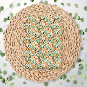 May include: A white background with a woven straw placemat. On top of the placemat is a printed sheet of paper with a repeating pattern of orange slices and green leaves.