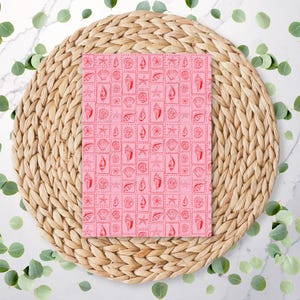 May include: A pink card with a repeating pattern of red seashells and starfish. The card is on a woven straw placemat.