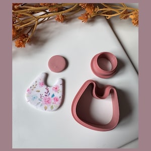 May include: A selection of polymer clay earring components. Features a floral patterned earring, a solid pink circle, a pink ring, and a pink earring cutter. The floral earring has a white base with pink and blue flowers.