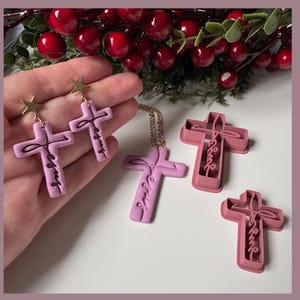 May include: A selection of cross-shaped jewellery and craft items. The jewellery includes earrings and a necklace, all featuring a cross design with the word "Jesus". The craft items are cross-shaped cookie cutters. The crosses are light purple.