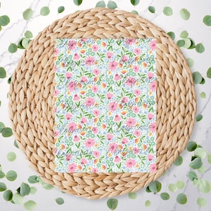 May include: A white background with a woven wicker coaster. On top of the coaster is a square piece of fabric with a floral pattern in pink, blue, yellow, and green.
