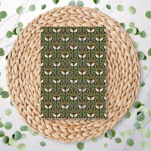 May include: A rectangular patterned design with a repeating motif of white butterflies and green leaves on a dark green background. The design is on a round, woven, light brown placemat, with scattered green leaves around it.