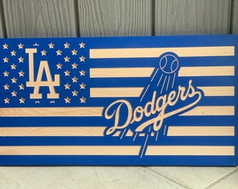 May include: Wooden wall art featuring the design of the American flag with the Los Angeles Dodgers logo. The flag has blue stripes and a blue field with stars, and the Dodgers logo is prominently displayed.
