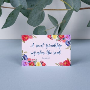 Puede incluir: Una tarjeta rosa con un borde floral y la cita "¡Una dulce amistad refresca el alma!" con el texto "Proverbios 17:17" debajo.