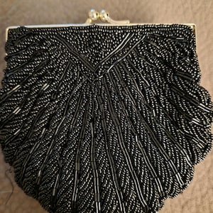 May include: A black beaded coin purse featuring a shell-like shape with intricate rows of small black seed beads and elongated tube beads arranged in a radiating pattern. The purse has a silver-toned metal frame with a kiss-lock closure.