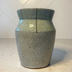May include: A light gray ceramic vase with a speckled glaze and dark gray stripes around the rim.