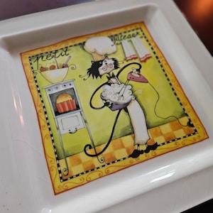 May include: White ceramic square dish with a colorful illustration of a cat wearing a chef's hat and apron, baking in a kitchen. The text "petit gateau" is written on the dish.