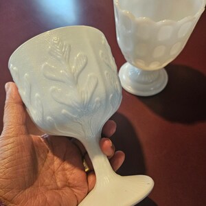 Puede incluir: Dos jarrones de vidrio de leche blanco con diseños en relieve. Un jarrón tiene un borde festoneado y un patrón de lunares. El otro jarrón tiene un diseño de árbol.