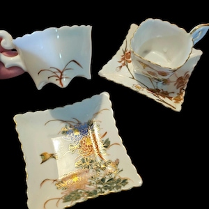 May include: A set of three white porcelain pieces with scalloped edges. The set includes a teacup, a saucer, and a small square dish. The teacup and saucer have gold trim and floral designs. The square dish features a bird and floral design.