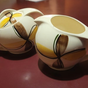 May include: A set of two white ceramic creamer and sugar bowls with a geometric design in yellow, brown, and green.