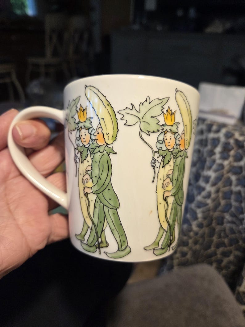 May include: White ceramic mug with a whimsical illustration of figures in green suits and yellow hats. The figures are holding long, yellow objects and walking. The mug has a curved handle.