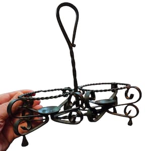 May include: A dark metal candle holder with a handle. The holder has two circular spaces for candles, with decorative swirls and a twisted metal design. The handle is a loop shape.