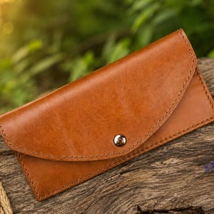 May include: A rectangular tan leather wallet featuring a curved flap closure secured with a single silver-toned metal snap button. The wallet has visible stitching along the edges and a smooth, consistent finish across the front surface.