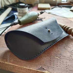 Może przedstawiać: Etui na okulary wykonane z ciemnoniebieskiej skóry z klapką i ozdobnymi szwami. Etui jest przeznaczone do przechowywania okularów korekcyjnych lub przeciwsłonecznych.