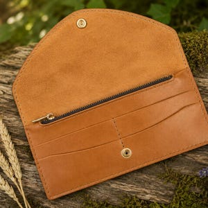 Peut inclure: Un portefeuille enveloppe en cuir beige doté d'un rabat pointu avec une fermeture à pression dorée. L'intérieur comprend un compartiment zippé avec une tirette dorée, plusieurs fentes horizontales pour cartes et un bouton-pression assorti.
