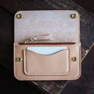 May include: A light brown leather wallet with a zipped pocket and a card slot. The wallet is open and the inside is visible.