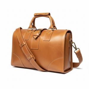 May include: A tan leather duffel bag with a top handle and a detachable shoulder strap. The bag has a rectangular shape with rounded corners, a buckle closure, and brass-coloured hardware. The bag is designed for travel and has a classic, timeless style.