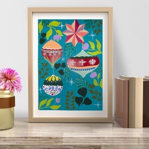 May include: Framed artwork featuring colorful Christmas ornaments and a star against a teal background. The ornaments are red, orange, and yellow with intricate designs. Green leaves and purple flowers add to the festive holiday theme. The frame is a light beige color.