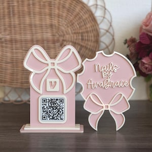 May include: Pink and white wooden sign with a bow and a QR code. The sign says "Nails by Ava Grace".