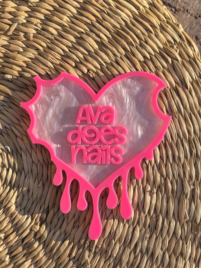 Pode incluir: Uma bandeja de resina em forma de cora&ccedil;&atilde;o rosa com um design de m&aacute;rmore branco e o texto "Ava does nails" em letras rosa. A bandeja tem um efeito de gotejamento na parte inferior.