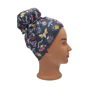 May include: A dark gray fabric head wrap with a colorful bug and butterfly print. The wrap is tied in a bun on top of the head.