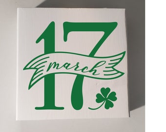 May include: Green wooden sign with the numbers 17 and the word "march" in a banner. A green four-leaf clover is in the bottom right corner.