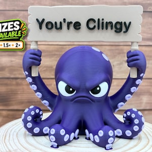 May include: A purple octopus figurine with a grumpy expression, holding a beige rectangular sign that reads "You're Clingy" in black text. The octopus has light purple suckers on its tentacles and a sticker indicating 3 sizes are available.