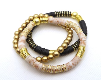 May include: Set of three bracelets featuring gold, black, and cream colored beads. The bracelets are stacked on top of each other.