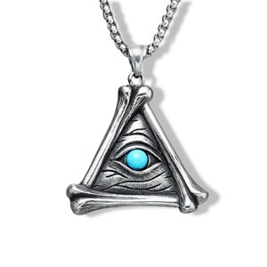 Puede incluir: Collar con colgante plateado con un diseño triangular con un ojo y un centro de color turquesa. El colgante está enmarcado por estructuras óseas y cuelga de una cadena. Fondo blanco.