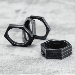 May include: A collection of dark grey, hexagonal rings. The rings are stacked and scattered on a light grey surface. The rings have a weathered, metallic appearance, suggesting a vintage or industrial style.