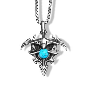 May include: A silver-toned metal pendant necklace featuring a central round turquoise stone with dark veining. The pendant has a symmetrical, pointed design with wing-like extensions and intricate engraved details, suspended from a box chain.