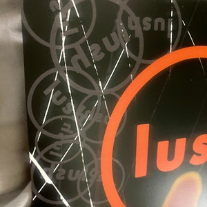 Pode incluir: Um gr&aacute;fico preto e branco com a palavra "lush" repetida em um padr&atilde;o circular. A palavra "lush" est&aacute; em um c&iacute;rculo grande de cor laranja.