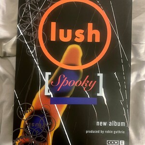 Pode incluir: Um cartaz preto e branco com um grande c&iacute;rculo laranja contendo a palavra "lush" em texto branco. O c&iacute;rculo &eacute; rodeado por c&iacute;rculos menores com a palavra "lush" em texto preto. O cartaz tamb&eacute;m apresenta o texto "Spooky" em texto branco dentro de um ret&acirc;ngulo branco. O texto "new album" e "produced by robin guthrie" tamb&eacute;m est&atilde;o inclu&iacute;dos em texto branco. O cartaz inclui o logotipo 4AD e o texto "1991 reprise records." e "tip for hi-fi listeners: play this one loud, it'll sound better."