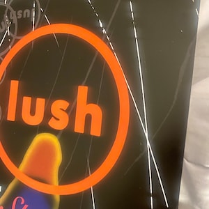 Pode incluir: Um cartaz preto e branco com um grande c&iacute;rculo laranja em torno da palavra "lush" em letras brancas. O cartaz tamb&eacute;m tem a palavra "Spooky" em letras brancas com um fundo azul e roxo.