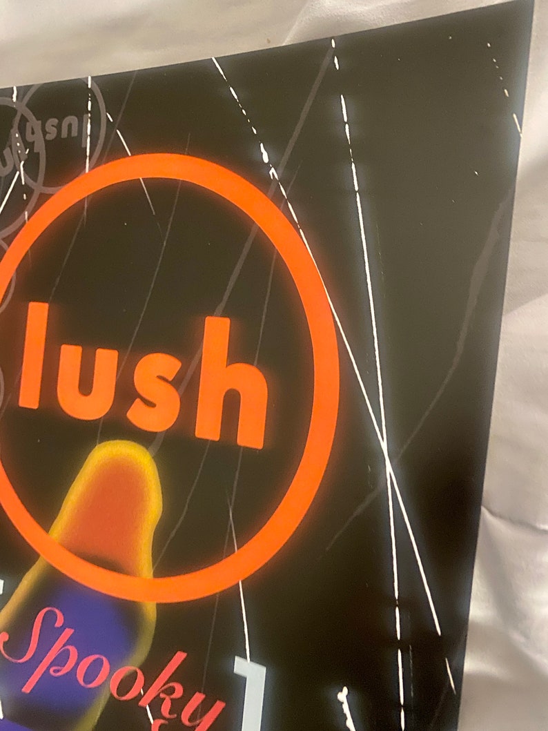 Pode incluir: Um cartaz preto e branco com um grande c&iacute;rculo laranja em torno da palavra "lush" em letras brancas. O cartaz tamb&eacute;m tem a palavra "Spooky" em letras brancas com um fundo azul e roxo.