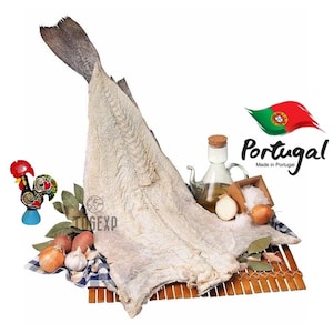 May include: Dried codfish, also known as bacalhau, is a traditional Portuguese food. The codfish is white and flaky, and it is displayed on a wooden surface with a Portuguese flag and other ingredients.