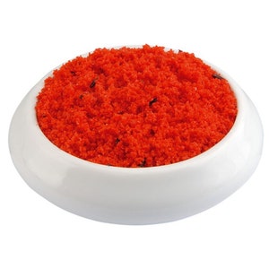 May include: A small white bowl filled with bright red, finely ground spice.