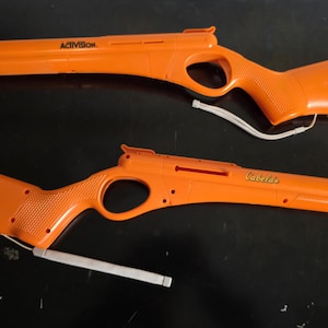 May include: Two orange plastic toy rifles. One rifle has the word "ACTIVISION" printed on the side. The other rifle has the word "Cabela's" printed on the side. Both rifles have a white cord attached.