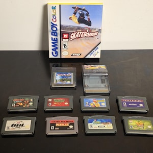 Könnte beinhalten: Eine Game Boy Color Videospielverpackung für Skateboarding mit einem Skater in der Luft, zusammen mit zehn verschiedenen Game Boy Color Spielmodulen. Die Module sind grau und durchscheinend, jedes mit einem individuellen Etikett versehen.