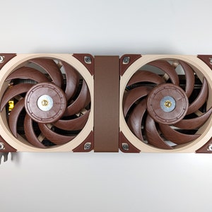 Könnte beinhalten: Eine beige und braune Grafikkarte mit zwei großen Lüftern. Die Lüfter haben braune Flügel und eine silberne Mitte.