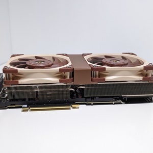 Puede incluir: Una tarjeta gr&aacute;fica beige y marr&oacute;n con dos ventiladores. Los ventiladores tienen un marco beige y aspas marrones.