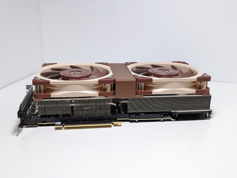 Puede incluir: Una tarjeta gr&aacute;fica beige y marr&oacute;n con dos ventiladores. Los ventiladores tienen un marco beige y aspas marrones.