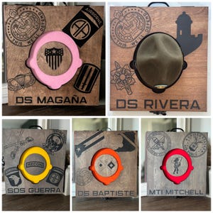 May include: Wooden display boxes with various military emblems and text. Each box features a circular cutout with a colored insert, and the names "DS MAGAÑA", "DS RIVERA", "SDS GUERRA", "DS BAPTISTE", and "MTI MITCHELL" are displayed.