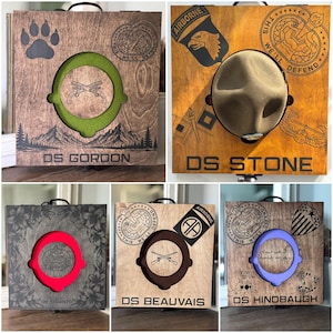 May include: Five square wooden display cases for drill sergeant hats, each featuring a central circular cutout, a handle, and engraved military-themed graphics including unit insignias, paw prints, floral patterns, and names like DS GORDON and DS STONE.