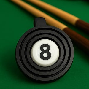 May include: A black and white eight ball with a black handle, set against a green background. Two pool cues are visible in the background. The eight ball is the focal point, with the number "8" prominently displayed.