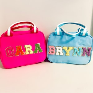 May include: Two personalized zippered lunch bags. One is pink with the name "CARA" in colorful letters. The other is blue with the name "BRYNN" in colorful letters.