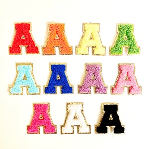 May include: Twelve felt letter patches in various colors, each with a gold outline. The letters are all the letter 'A' and are arranged in three rows of four.